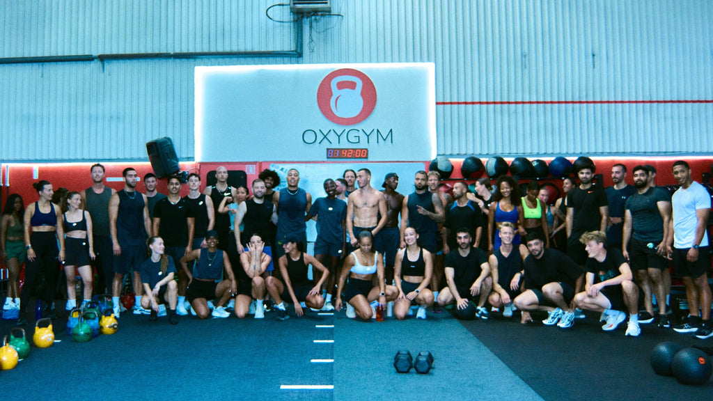 Group of people posing for a photo at TRANSCEND YOUR LIMITS WORKOUT in a gym with Oxygym branding. SCEND WORKOUT 