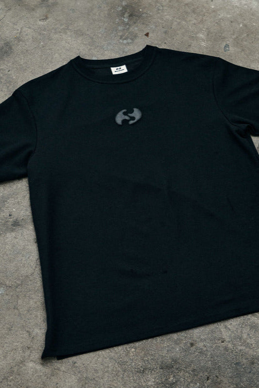 Black t-shirt with a logo on a concrete surface